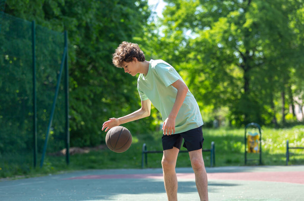 10代のバスケットボールの笑顔、陽気な演奏。バスケットボールボールを屋外で男の子にフィット。子供がコートでボールをドリブル - 写真・画像