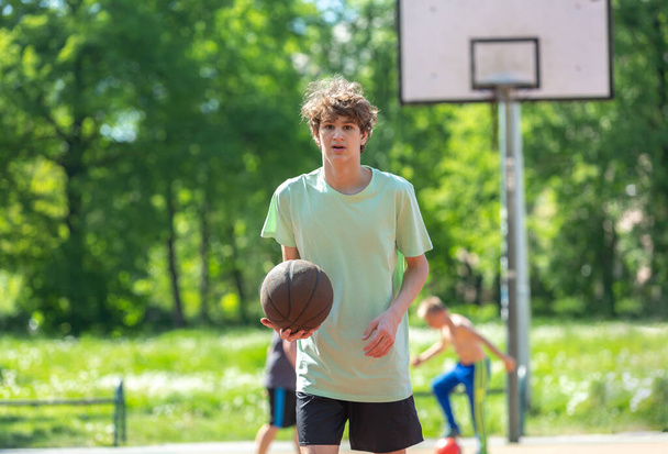 Teenager beim Basketballspielen lächelnd, fröhlich. Fit Junge mit Basketballball im Freien. Kind dribbelt den Ball auf dem Platz - Foto, Bild