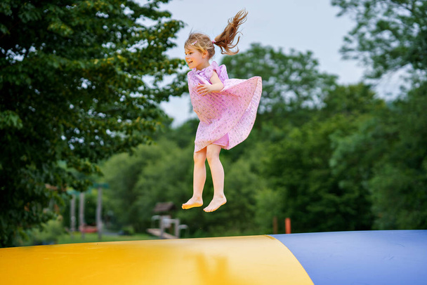 Pieni esikoulutyttö hyppää trampoliinilla. Hauskaa hauska lapsi hauskaa ulkona toimintaa kesällä. Urheilu ja harjoitukset lapsille. Trampolin Ukrainan lippu värit. - Valokuva, kuva