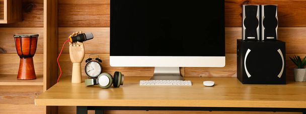 Arbeitsplatz mit modernem Computer, Lautsprechern und Mikrofon in der Nähe der Holzwand - Foto, Bild
