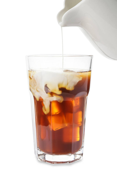 Melk gieten in glas met koude koffie op witte achtergrond, close-up - Foto, afbeelding