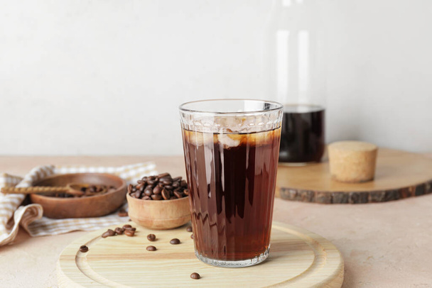 Vidrio con cerveza fría y granos de café sobre tabla de madera sobre fondo claro - Foto, Imagen