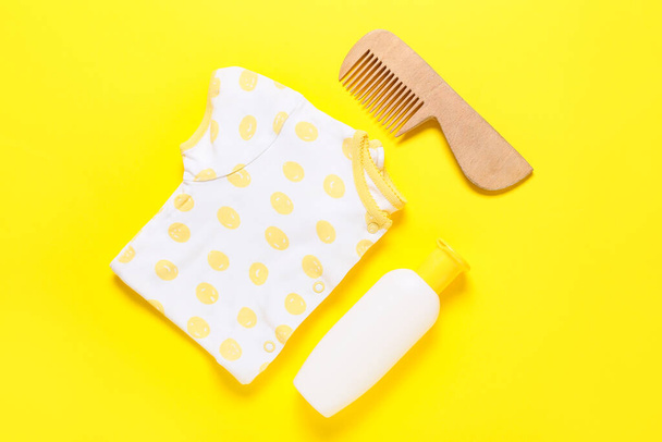 Traje de bebé, peine de madera y biberón con producto cosmético sobre fondo amarillo - Foto, Imagen