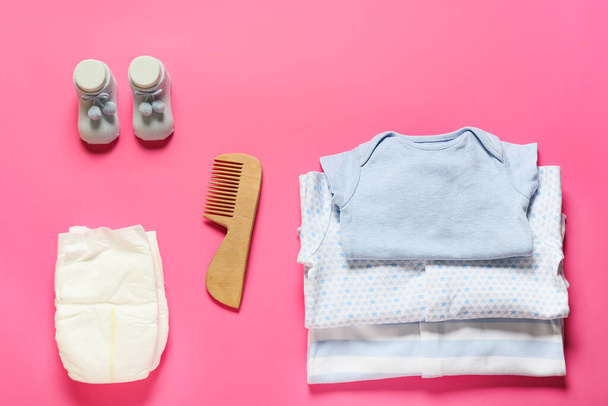 Ubrania dla niemowląt, pieluchy i drewniany grzebień do włosów na różowym tle - Zdjęcie, obraz