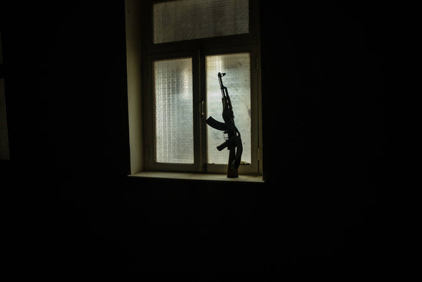 Концептуальное фото войны между Россией и Украиной. Русское оружие (винтовка) на подоконнике ночью. Старая жуткая комната с окном. Взрыв снаружи. - Фото, изображение