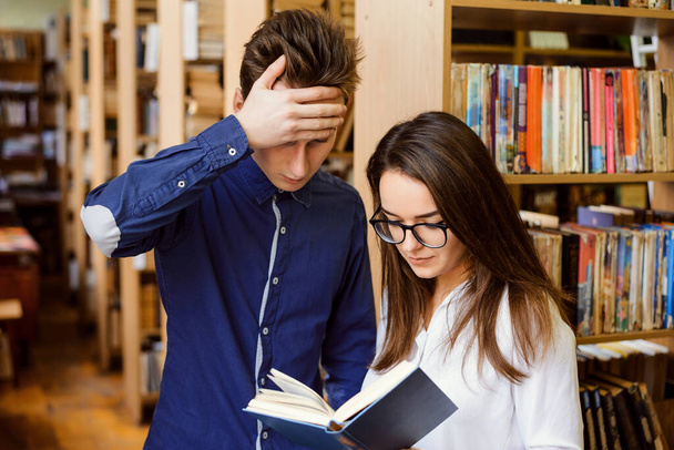 Dos estudiantes molestos en la biblioteca leyendo material para las clases, no pueden entenderlo, tratando de averiguar su significado - Foto, imagen