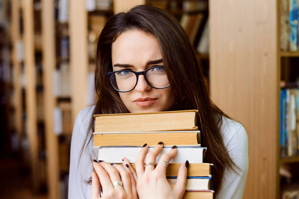 Tired female student in library with a lot of books preparing for exams - Foto, Bild