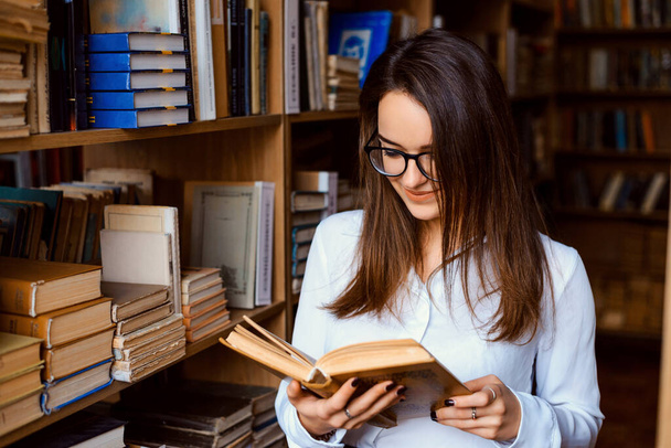 Młoda atrakcyjna studentka czytająca książkę w bibliotece - Zdjęcie, obraz