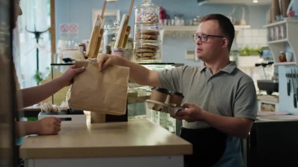 Hombre caucásico con síndrome de Down regalando comida para llevar a una clienta. Fotografía con cámara de helio RED en 8K.  - Metraje, vídeo