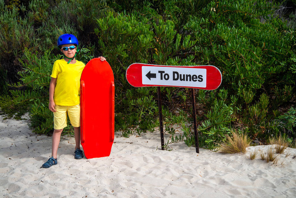 Petit garçon est prêt pour le sandboard à partir de dunes de sable tout en posant à côté du panneau, Kangaroo Island, Australie du Sud - Photo, image