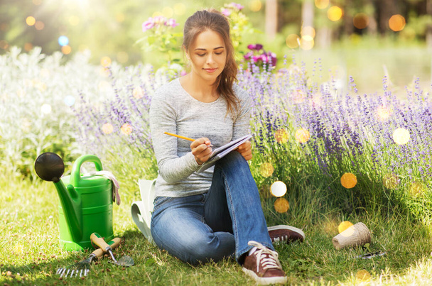 gardening and people concept - young woman writing to notebook at summer garden - Foto, immagini