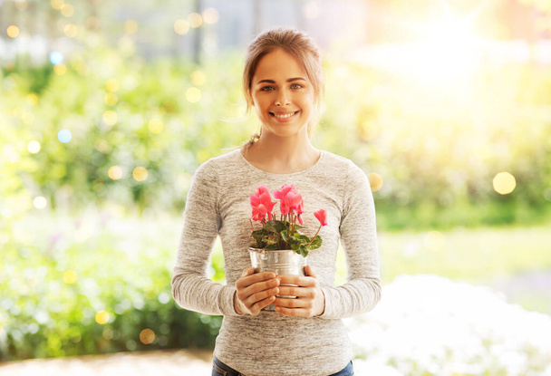 farming, gardening and people concept - happy young woman with pink cyclamen flowers in pot at summer garden - Fotoğraf, Görsel