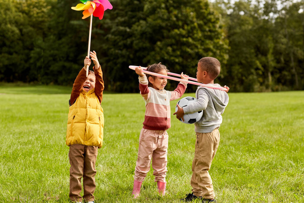 childhood, leisure and people concept - happy kids with pinwheel having fun at park - Foto, imagen