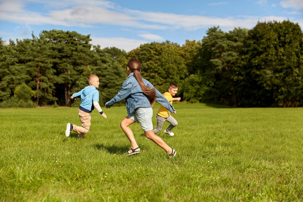 childhood, leisure and people concept - group of happy kids playing tag game and running at park - Foto, Bild