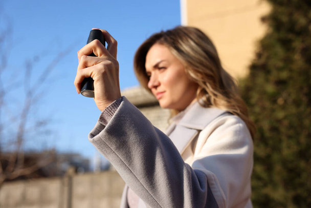 Young woman using pepper spray outdoors, focus on hand - Photo, Image