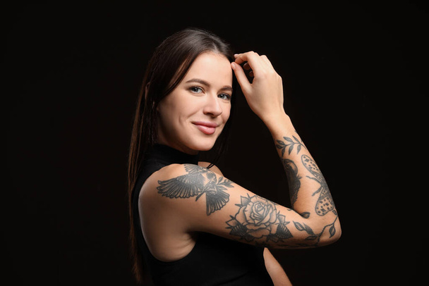 Beautiful woman with tattoos on arm against black background - Foto, afbeelding