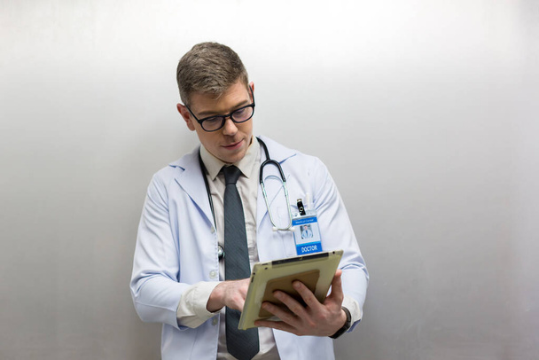 Doctor holding tablet at hospital. Friendly male doctor dressed in uniform holding tablet. - 写真・画像