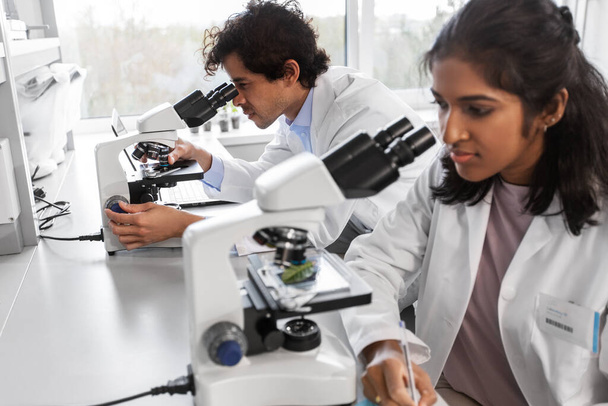 investigación científica, trabajo y concepto de personas - equipo internacional de científicos con microscopios que trabajan en laboratorio - Foto, imagen