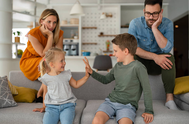Tired parents sitting on couch feels annoyed exhausted while happy children playing together at home - Φωτογραφία, εικόνα