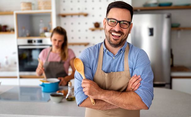 Portrait of handsome young happy man cooking at home preparing food in kitchen. - 写真・画像
