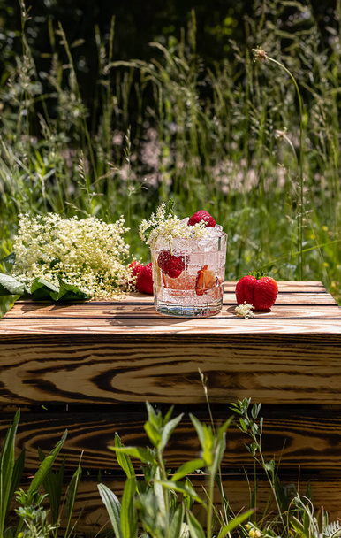 Sommerlimonade aus Holunderblüten und Erdbeeren. Ein kühles Erfrischungsgetränk auf der Holzkiste. Vertikale Orientierung.  - Foto, Bild