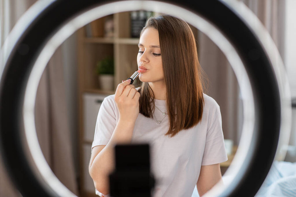 beauty blogging, make up and people concept - girl blogger with ring light and smartphone applying lipstick at home - Zdjęcie, obraz