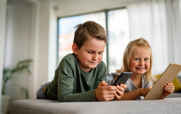Little girl and boy watching video or playing games on their digital device tablet, smartphone. Children digital addiction concept. - Photo, Image