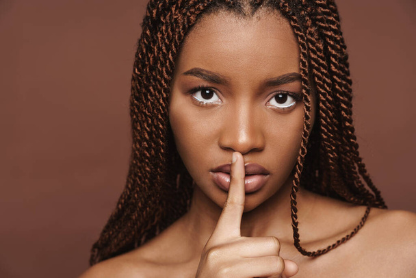 Half-naked black woman showing silence gesture at camera isolated over brown background - Foto, afbeelding