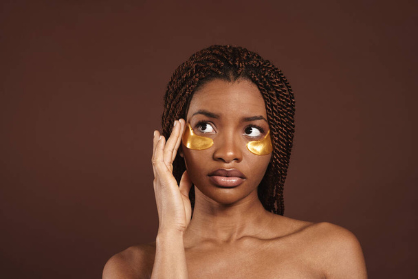 Half-naked black with pigtails woman posing in eye patches isolated over brown background - Photo, Image