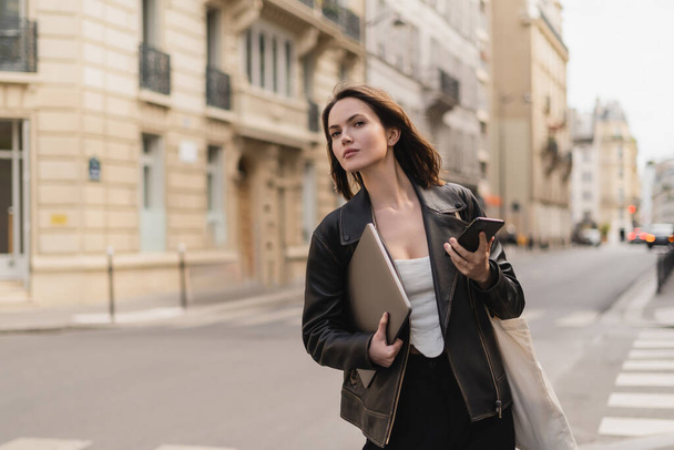 パリの路上でラップトップとスマートフォンを保持黒革のジャケットでスタイリッシュなフリーランサー - 写真・画像