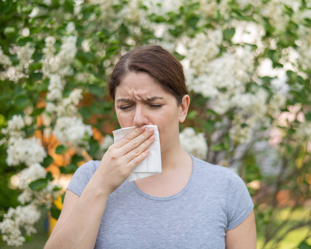 Valkoihoinen nainen kärsii allergioista ja puhaltaa nenänsä lautasliinaan kävellessään puistossa. - Valokuva, kuva