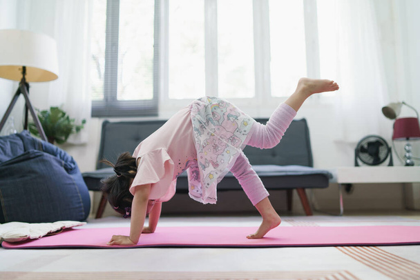 Asijské dívka dítě cvičení podle praxe YOGA držení těla v obývacím pokoji. - Fotografie, Obrázek