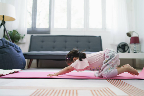 Азійська дівчинка займається фізичними вправами, практикуючи позу YOGA у вітальні.. - Фото, зображення