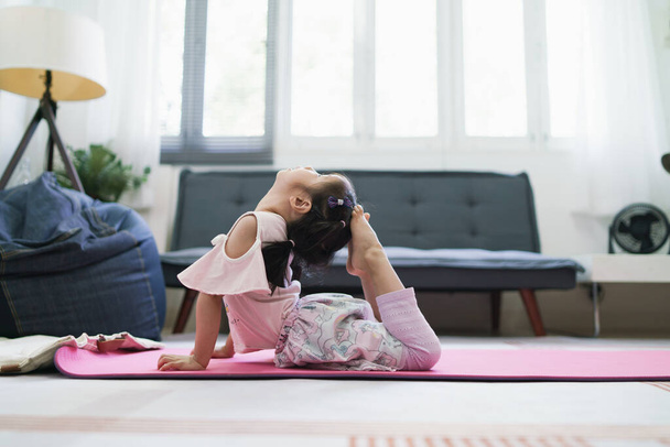 Азійська дівчинка займається фізичними вправами, практикуючи позу YOGA у вітальні.. - Фото, зображення