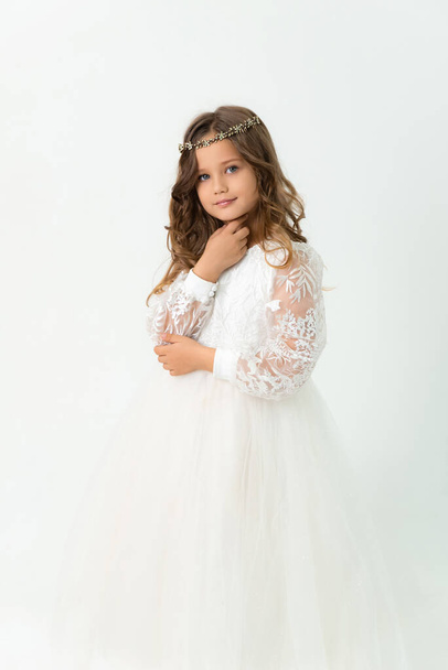 A little blonde girl in a white dress is looking at the camera. Studio portrait - Photo, image
