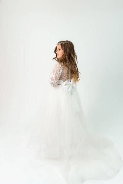 Маленькая девочка с красивой прической и белым платьем смотрит в сторону. Студийный портрет - Фото, изображение