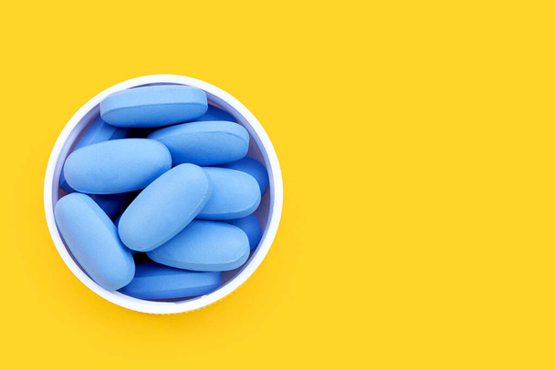 PrEP (Pre-Exposure Prophylaxis) niebieskie tabletki stosowane w celu zapobiegania HIV Niebieskie tabletki w plastikowych zakrętek butelki na żółtym tle. - Zdjęcie, obraz