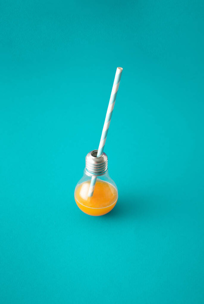 Energie pomerančový nápoj ve žárovce s pruhovanou pitnou slámou na modrém pozadí. - Fotografie, Obrázek