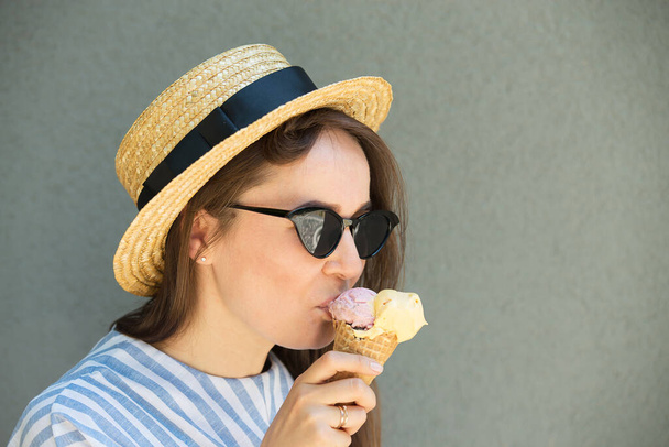 girl hipster in straw hat is eating ice cream next to gray wall - Photo, Image