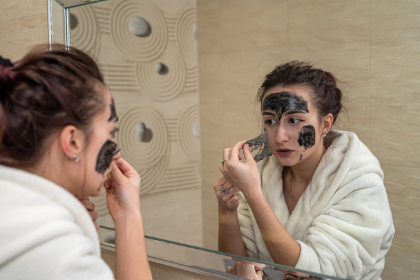 krásná mladá dívka dělá černou masku pro akné na obličeji. Koncept akné masky - Fotografie, Obrázek