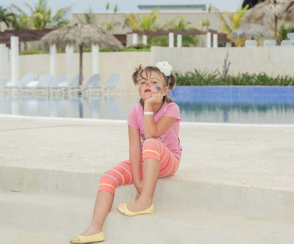 niña infeliz con la cara pintada sentado en escalones de hormigón cerca de la piscina en el fondo
 - Foto, Imagen