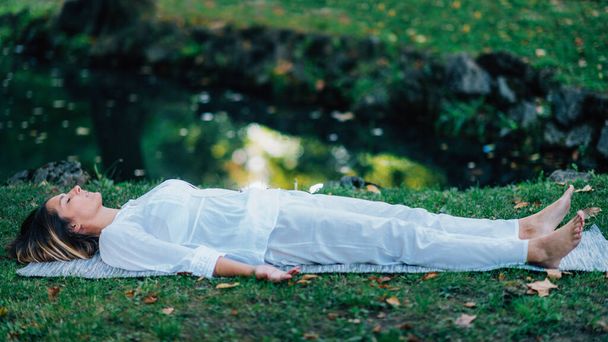 Corpse Position, Savasana, Meditation. Young woman practicing yoga and meditating by the water. - Photo, Image
