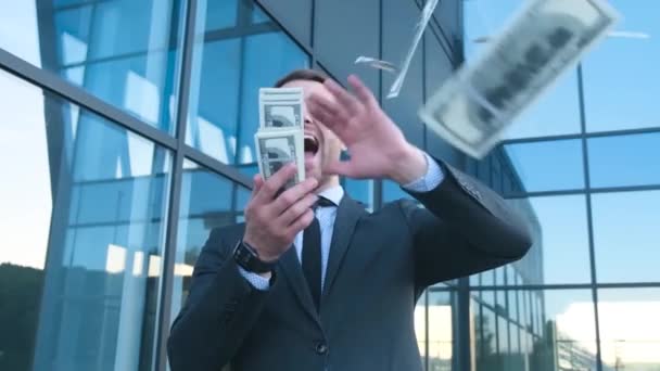 Verrückter Geschäftsmann wirft Geld in die Luft, er ist in der Nähe des Büros. Zeitlupe. Europäischer Geschäftsmann mit Dollars in der Hand - Filmmaterial, Video