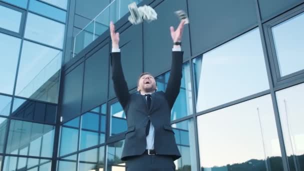 Rahaa, sadetta, voittoa, vaurautta. Onnellinen, hymyilevä valkoihoinen liikemies, joka sirottelee dollareita seistessään lähellä liikekeskusta. Liiketoiminnan ja rahan käsite - Materiaali, video
