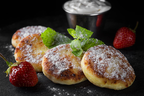 Cottage cheese pancakes with mint and sour cream, strawberries and powder. Black background, horizontal - Zdjęcie, obraz