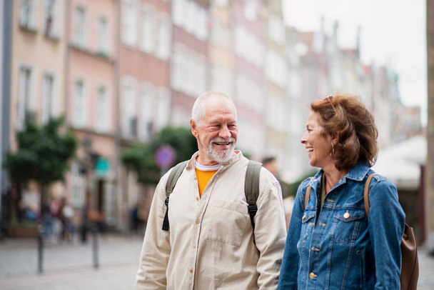 A portrait of happy senior couple tourists using smartphone outdoors in historic town - Фото, изображение