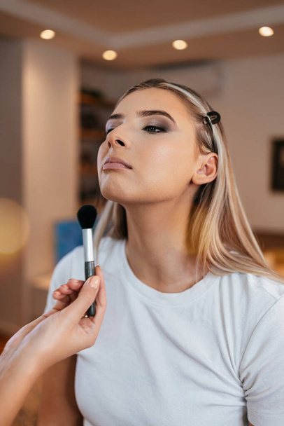 Makeup process. Professional artist applying make up on model face. Close up portrait of beautiful blonde woman in beauty saloon. - Foto, Imagen