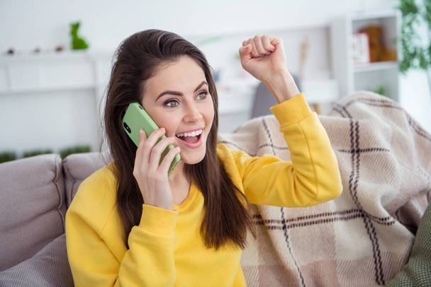 Portrait of attractive trendy cheerful girl sitting on divan talking on phone rejoicing good news at home indoors. - 写真・画像