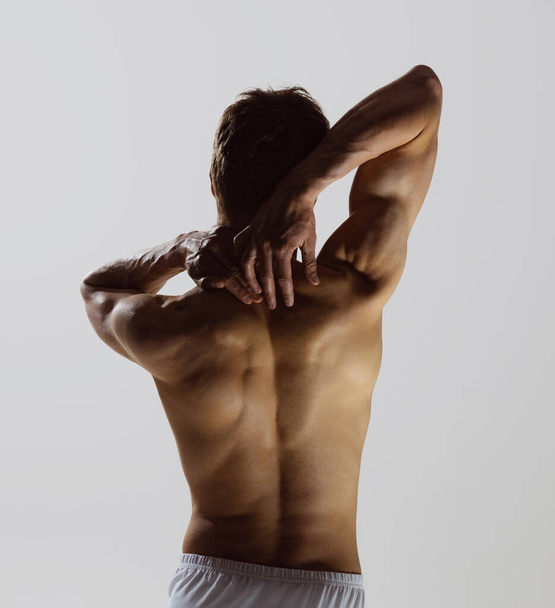 Model silhouette. Back view of young shirtless muscled man wearing white boxer-briefs standing isolated on gray background. Wellness, wellbeing, fitness, sport concept. Natural beauty of male body - Photo, Image