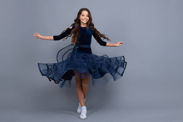 Full length teenager with movement dress. Young teen child with flowing skirt. Teen girl fluttering ball dress in motion, isolated on gray. Happy girl face, positive and smiling emotions - Photo, Image